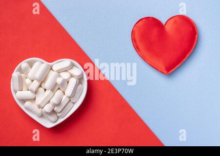 Pillen in Schale und rotes Herz auf blauem und rotem Hintergrund. Medikamente für Kardiologie Gesundheit Behandlung und Krankheiten. Stockfoto