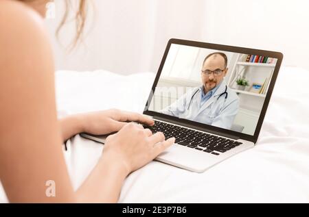 Nicht erkennbare weibliche Patientin, die online medizinische Dienste erhält und von zu Hause aus mit dem Arzt auf ihrem Laptop konsultiert wird Stockfoto