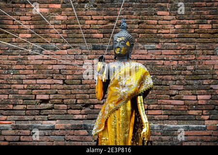 Eine Buddha-Statue trägt eine verzierte goldene Robe, mit heiligen Fäden, bekannt als Sai Sin um das Handgelenk befestigt. Diese verbinden die Mönche mit dem Heiligen Stockfoto