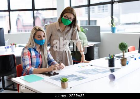 Zwei verschiedene Geschäftsfrauen tragen Gesichtsmasken Blick auf Blaupausen und Diskutieren Stockfoto