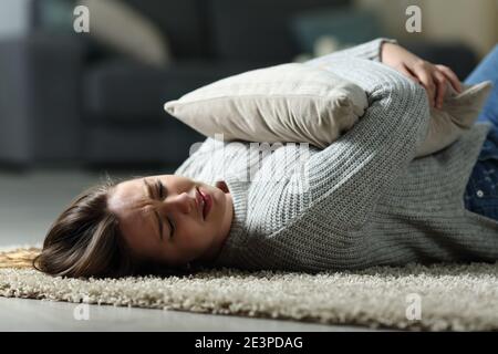 Trauriger Teenager, der sich beschwert, das Kissen umarmt und weint und auf dem liegt Boden zu Hause Stockfoto