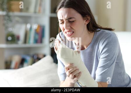 Frau mit verletztem schmerzhaftem Arm, die sich auf einer Couch beschwert Im Wohnzimmer zu Hause Stockfoto