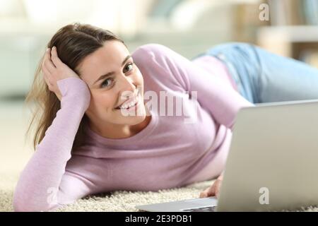 Glückliche Frau mit Laptop, die Sie auf dem liegend ansieht Boden zu Hause Stockfoto