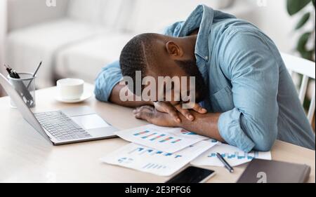 Schlafen Bei Der Arbeit. Erschöpfter schwarzer Freiberufler, der am Schreibtisch im Heimbüro nippt Stockfoto
