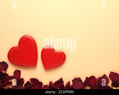 Rustikale Holzherzen mit Rosenblättern auf gelbem Hintergrund mit Leerzeichen für Text Stockfoto