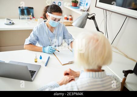 Doktor schreibt in ihr Notizbuch für eine ältere Patientin Stockfoto