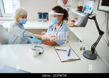 Arzt, der eine Druckmanschette an einen Rentner-Arm legt Stockfoto