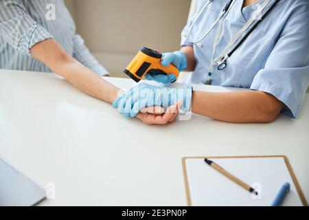 Medic mit einer Temperaturpistole an einem Arm eines gealterten Patienten Stockfoto