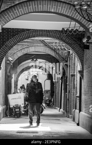 Ein alter Mann, der in einer Gasse traditioneller Shikumen-Häuser an der zentralen Huai Hai Road, einer der Haupteinkaufsstraßen in Shanghai, raucht. Stockfoto