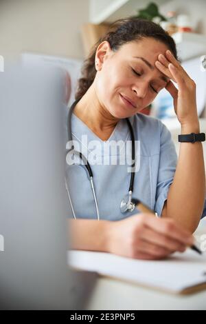 Müde Arzt schnappte sich ihren Kopf, während mit einem Stift Stockfoto