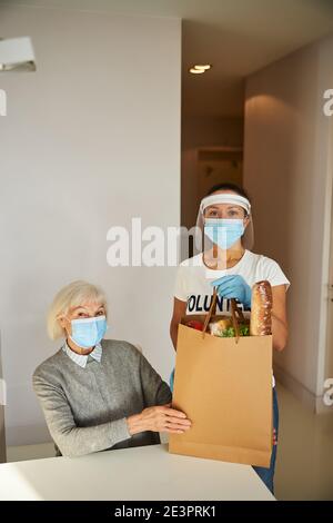 Weibliche Freiwillige neben dem sitzenden Rentner stehen Stockfoto