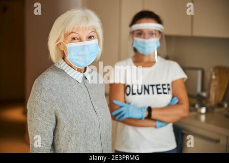 Volunteer in Latexhandschuhen hinter einer älteren Dame stehen Stockfoto