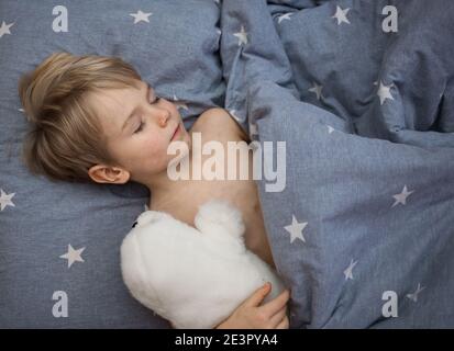 4-5 Jahre altes Kind schläft auf grauer Bettwäsche mit weißem Plüschtier im Arm. Süßer Schlaf von niedlichen Kleinkind Junge, gesunden Tagesschlaf, Kinderbetreuung. Gut Stockfoto