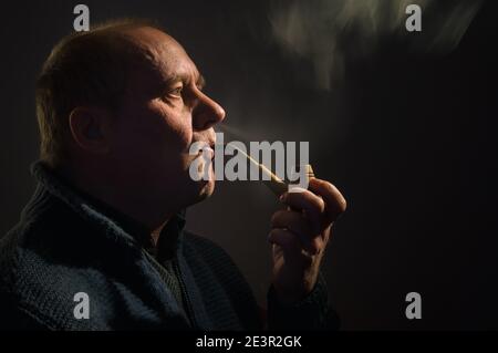 Schönes Porträt eines kaukasischen Mannes mit Tabakpfeife (Seitenansicht, Low Key) Stockfoto