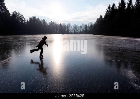 Silhouette eines Jungen Eislaufen auf gefrorenem See, von der Sonne von hinten bei Sonnenaufgang beleuchtet, Slowenien Stockfoto