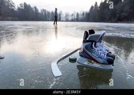 Männliche Schlittschuhe Hockey liegt auf einer Oberfläche von gefrorenen see mit Eis bedeckt mit einer weiblichen Skater in der Hintergrund Stockfoto