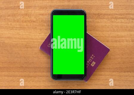 (Selektiver Fokus) AUF einem Holztisch SIND EIN Reisepass und ein Smartphone mit grünem Bildschirm angeordnet. Reisekonzept mit Kopierplatz. Stockfoto