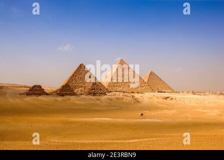 Nordafrika Ägypten Kairo Gizeh Stadtmann reitet Kamelreiter vor den Pyramiden Ägyptens in der Wüstenlandschaft blaue Himmelspyramiden der Stadt gizeh Stockfoto