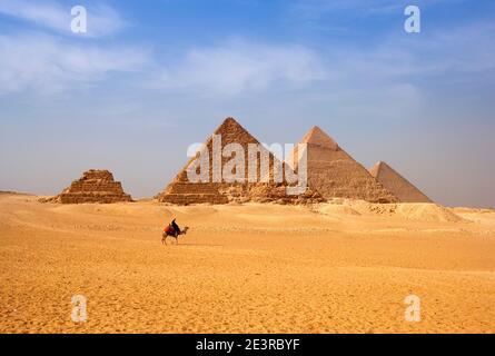 Nordafrika Ägypten Kairo Gizeh Stadtmann reitet Kamelreiter vor den Pyramiden Ägyptens in der Wüstenlandschaft blaue Himmelspyramiden der Stadt gizeh Stockfoto