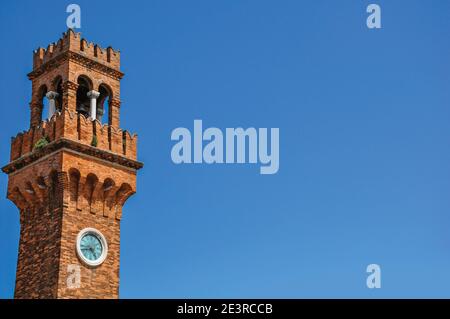 Detail des Uhrturms aus Ziegeln mit sonnigem blauen Himmel im Hintergrund bei Murano, einer kleinen und angenehmen Stadt in der Nähe von Venedig. Norditalien Stockfoto