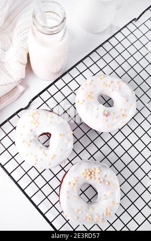 Donuts auf dem Backblech glasiert weiße Schokoladencreme oder Glasur und Flasche mit Milch auf dem Hintergrund Stockfoto