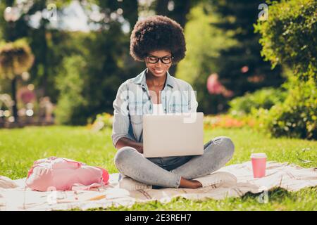 Foto-Porträt von schwarz gehäutet junge Studentin mit der Arbeit Computer sitzt im Park tragen Brille in der Nähe Tasche Tasse Heißgetränk Stockfoto