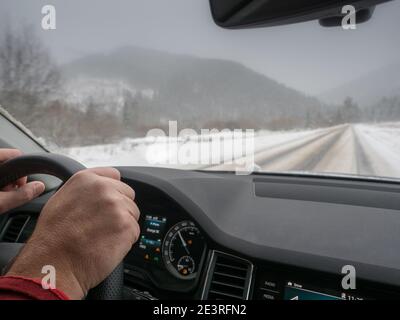 Fahren bei schneebedecktem Wetter. Blick aus dem Fahrerwinkel, während die Hände am Lenkrad liegen. Winterlandschaft. Stockfoto