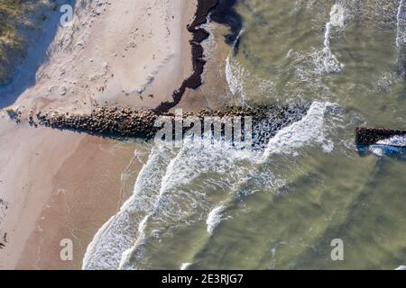 Luftaufnahme von oben nach unten von Wellen, die gegen alten Stein brechen Wellenbrecher Pier im Meer Stockfoto