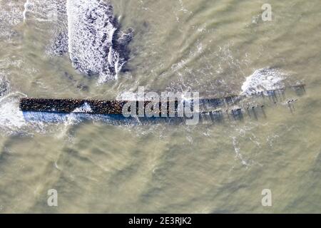 Luftaufnahme von oben nach unten von Wellen, die gegen alten Stein brechen Wellenbrecher Pier im Meer Stockfoto