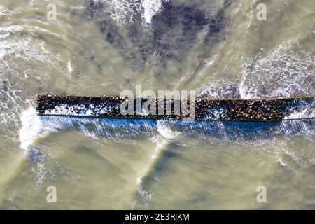 Luftaufnahme von oben nach unten von Wellen, die gegen alten Stein brechen Wellenbrecher Pier im Meer Stockfoto