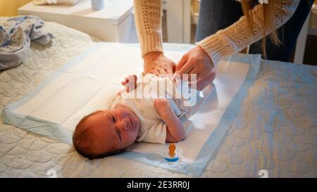 Junge Mutter ändert unordentliche Windeln zu ihrem neugeborenen Jungen weinend auf dem Bett in der Nacht. Konzept der Babyhygiene, liebevolle und fürsorgliche Eltern und Familie Stockfoto