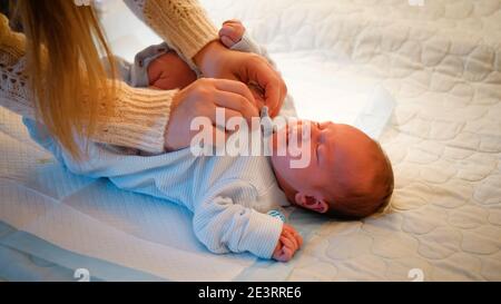 Draufsicht der Mutter, die ihr kleines neugeborenes Baby nachts auf dem Bett kleidet. Eltern ziehen Kleidung an und Knopfverschluss am Babybody. Konzept des Babys Stockfoto