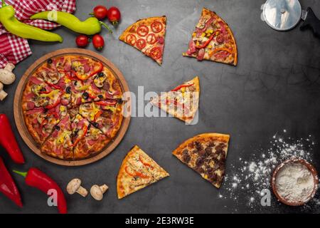 Pizzascheiben mit Thunfisch, Salami, Pilzen, Pepperoni und Gewürzen auf schwarzem Hintergrund, Kopierraum, Draufsicht Stockfoto
