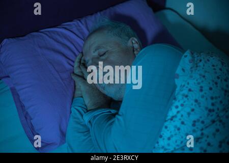 Älterer Mann, der mitten in der Nacht in einem Bett schläft, tief schlafen Stockfoto