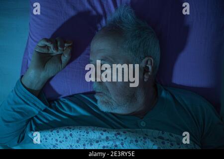 Älterer Mann, der mitten in der Nacht in einem Bett schläft, tief schlafen Stockfoto