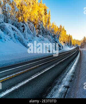 Eisige Autobahn durch einen schneebedeckten arktischen Wald an einem hellen Wintertag. Stockfoto