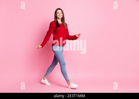 In voller Länge Profil Foto von niedlichen jungen Dame gehen aussehen Kamera tragen roten Pullover Jeans Sneakers isoliert rosa Farbe Hintergrund Stockfoto