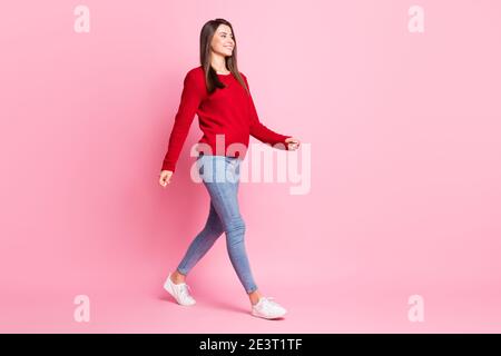 In voller Länge Profil Foto von schönen Mädchen zu Fuß tragen rot pullover Denim Jeans Sneaker isoliert rosa Farbe Hintergrund Stockfoto