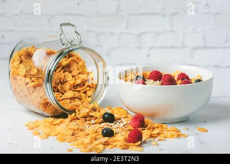 Gesundes Frühstück.Glas mit Getreide neben einer Schüssel Müsli, Cerealien, Himbeeren und Heidelbeeren auf Marmortisch Stockfoto