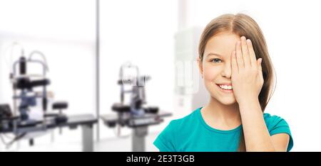 Lächelnd teen Mädchen schließen Auge mit ihrer Hand für die Überprüfung der Vision, über Hintergrund Augenheilkunde Klinik. Vision Test Konzept Stockfoto