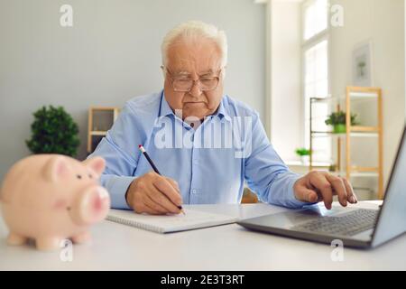 Pensionierter Mann mit Laptop und Notizen in Notebook studieren Pensionsplan und Verwaltung seines Budgets Stockfoto