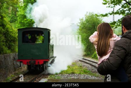 Ankunft mit Dampfzug. Attraktion für Kinder und Eltern. Azpeitia, Spanien. Vater hält Tochter, die Ohren wegen der lauten Lokpfeife schließt. Auswahl Stockfoto