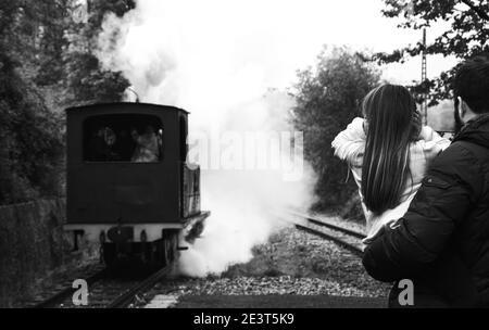 Ankunft der Dampfeisenbahn. Azpeitia, Spanien. Vater hält Tochter, die Ohren schließt, weil die Lokomotive laut pfeift. Historisches Foto in Schwarzweiß Stockfoto