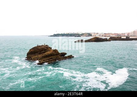 Biarritz (Frankreich). Blick vom Felsen der Jungfrau Maria auf Felsen mit Kreuz (zum Gedenken an ertrunkene Seeleute) im Meerwasser, Stadtstrand und Leuchtturm Stockfoto