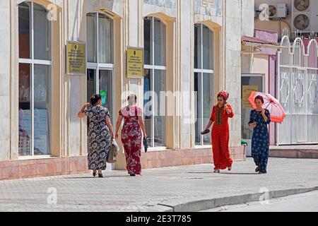 Turkmenische Frauen, die in der Hauptstadt Aschgabat, Turkmenistan, auf dem Bürgersteig spazieren, tragen ein Koynek, traditionelles langes Kleid mit Stickerei Stockfoto