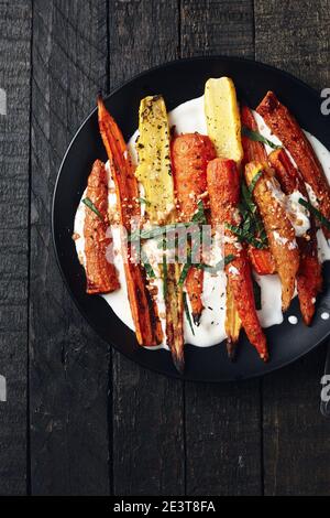 Salat aus gerösteten Karotten mit Joghurt, Gewürzen und Kräutern auf dunklem Grund. Stockfoto