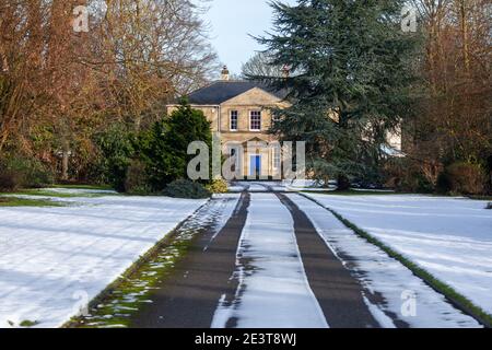 Eine lange gerade schneebedeckte Fahrt und Garten in Richtung Ein georgianisches Haus mit blauer Tür Stockfoto