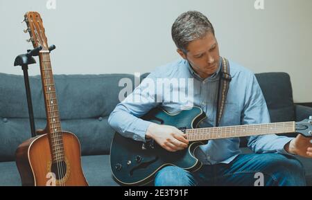 Gutaussehender Mann, der seine halbakustische Gitarre im Innenbereich anstimmt. Stockfoto