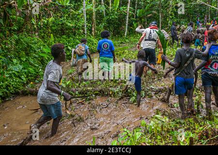 Ein Junge in einem T-Shirt mit dem Aufdruck "Black Brother" watet mit der Gruppe durch einen schlammigen Waldweg in der Nähe von Buin auf Bougainvillea, Papua-Neuguinea. Stockfoto