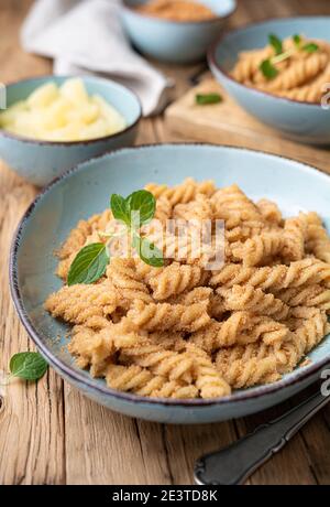 Einfache Fusilli-Pasta mit süß gebratenem Grieß und Zimt, serviert mit Ananasstücken Stockfoto